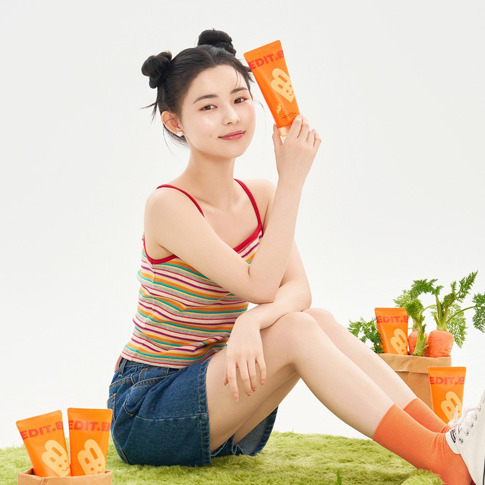 EDIT.B Joyful Carrot Foaming Gel Cleanser 150ml de la marque EDIT.B : femme tient le flacon, fond herbe, carottes visibles.
