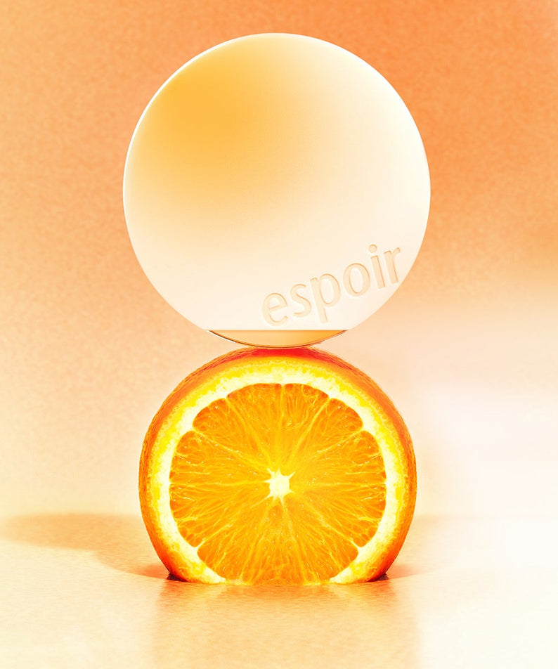 ESPOIR BE GLOW VOLUME CUSHION SPF42 PA+++ [Gleaming CALI Edition] étincelant devant une orange sur fond orange.