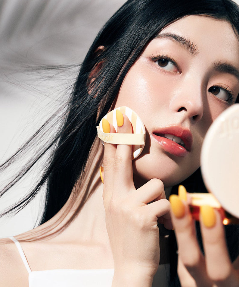 Femme utilisant ESPOIR BE GLOW VOLUME CUSHION SPF42 PA+++ [Gleaming CALI Edition] pour un teint lumineux en intérieur.