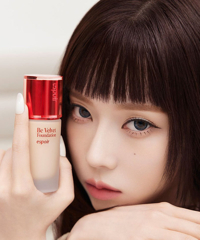 ESPOIR BE VELVET FOUNDATION SPF22 PA++ : la fondation en main, sur un visage maquillé, emballage rouge, fond clair.