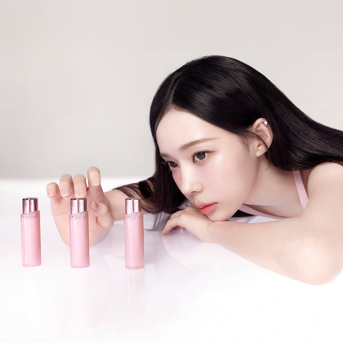 Modèle maquillage posant, ESPOIR Bare Glow Lip Balm à côté, marque ESPOIR en flacons roses sur fond clair.
