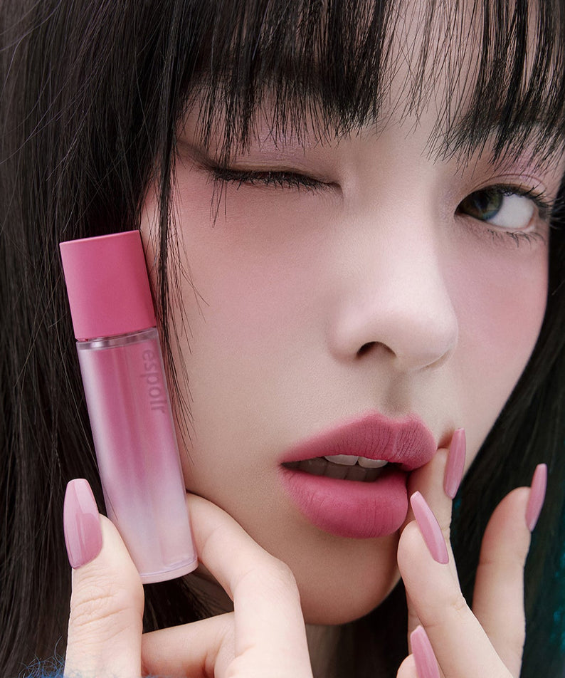 Femme appliquant ESPOIR Couture Lip Tint Fitting Blur avec un flacon rose, maquillage élégant et moderne, effet flouté.