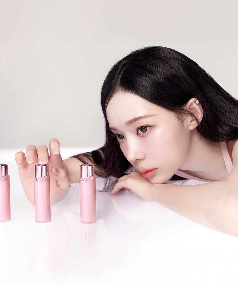 Femme contemplant l'ESPOIR Bare Glow Lip Balm en trois flacons roses, beauté et éclat naturel en vedette.