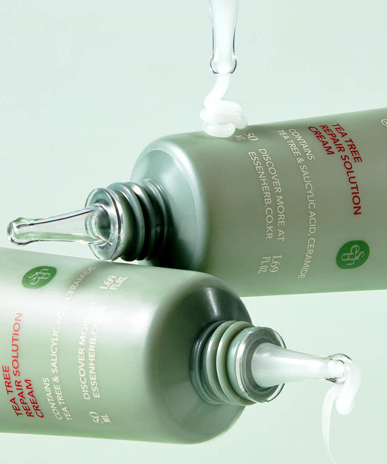 Deux bouteilles de ESSENHERB Tea Tree Repair Solution Cream 50ml ouvertes, avec de la crème coulant des tubes, sur un fond vert clair.