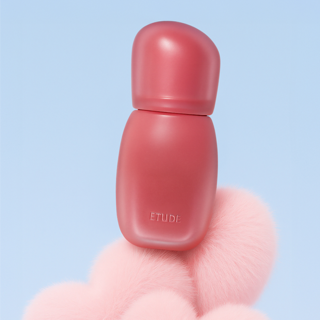 ETUDE Cozy Fixing Tint 4g de ETUDE, tube rosé sur fond bleu ciel, posé sur un accessoire duveteux rose.