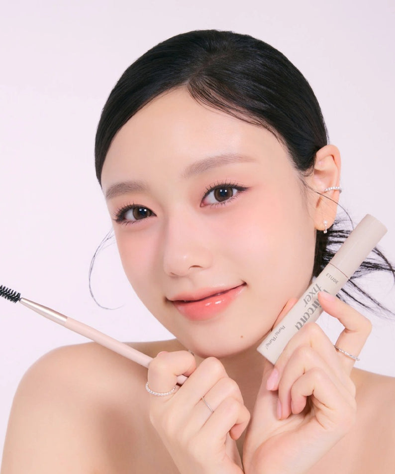 Femme souriante tenant ETUDE Pangpang Hair Cara Fixer 10ml et une brosse, mise en valeur des cheveux, produit de beauté capillaire.