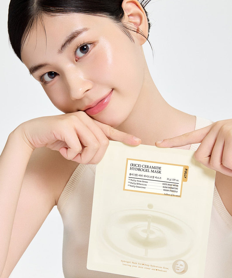Personne souriante appliquant FULLY Rice Cera Hydrogel Mask de la marque FULLY, masque hydrogel sur le visage, fond clair.