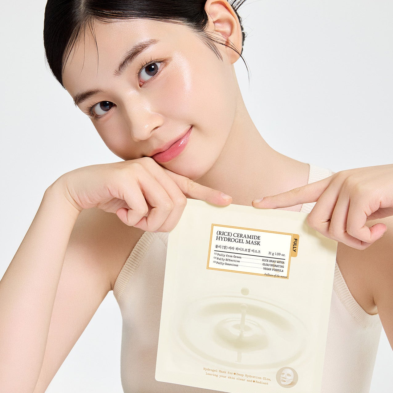 Personne souriante appliquant FULLY Rice Cera Hydrogel Mask de la marque FULLY, masque hydrogel sur le visage, fond clair.