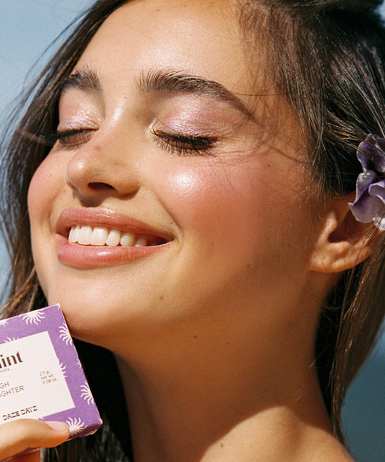 Femme souriante avec GLINT Glint Highlighter (Marble), maquillage éclatant et packaging en détail.