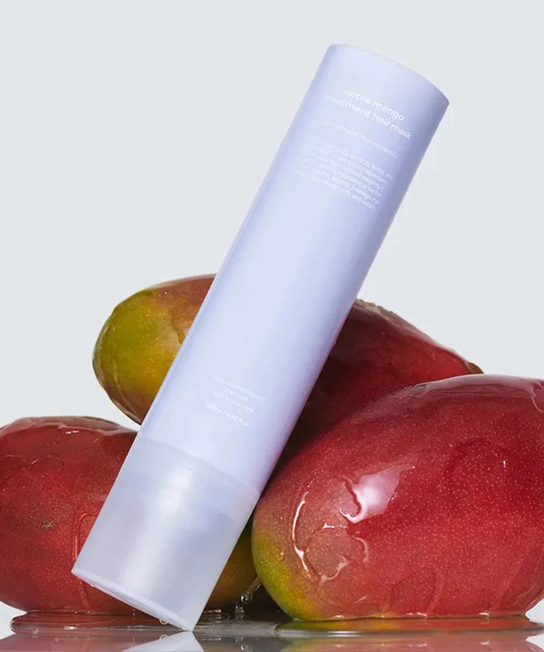 GLOW Apple Mango Hair Treatment 250ml par GLOW, flacon blanc sur pommes et mangues, fond clair, produit en gros plan.