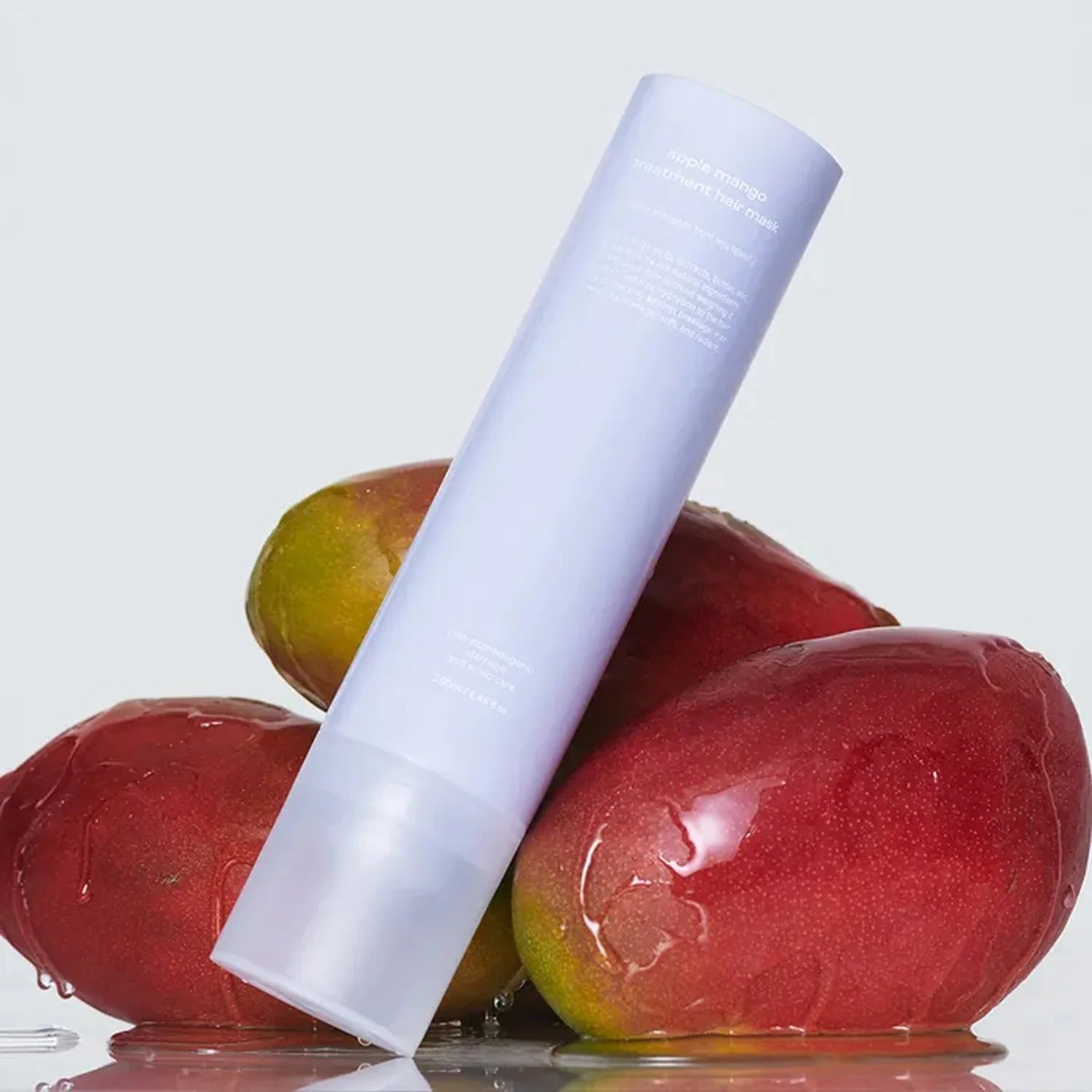 GLOW Apple Mango Hair Treatment 250ml par GLOW, flacon blanc sur pommes et mangues, fond clair, produit en gros plan.