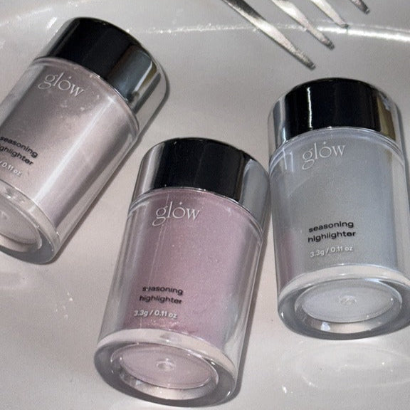 GLOW Seasoning Highlighter de la marque glōw, flacons lumineux sur fond argenté, ambiance maquillage glamour.