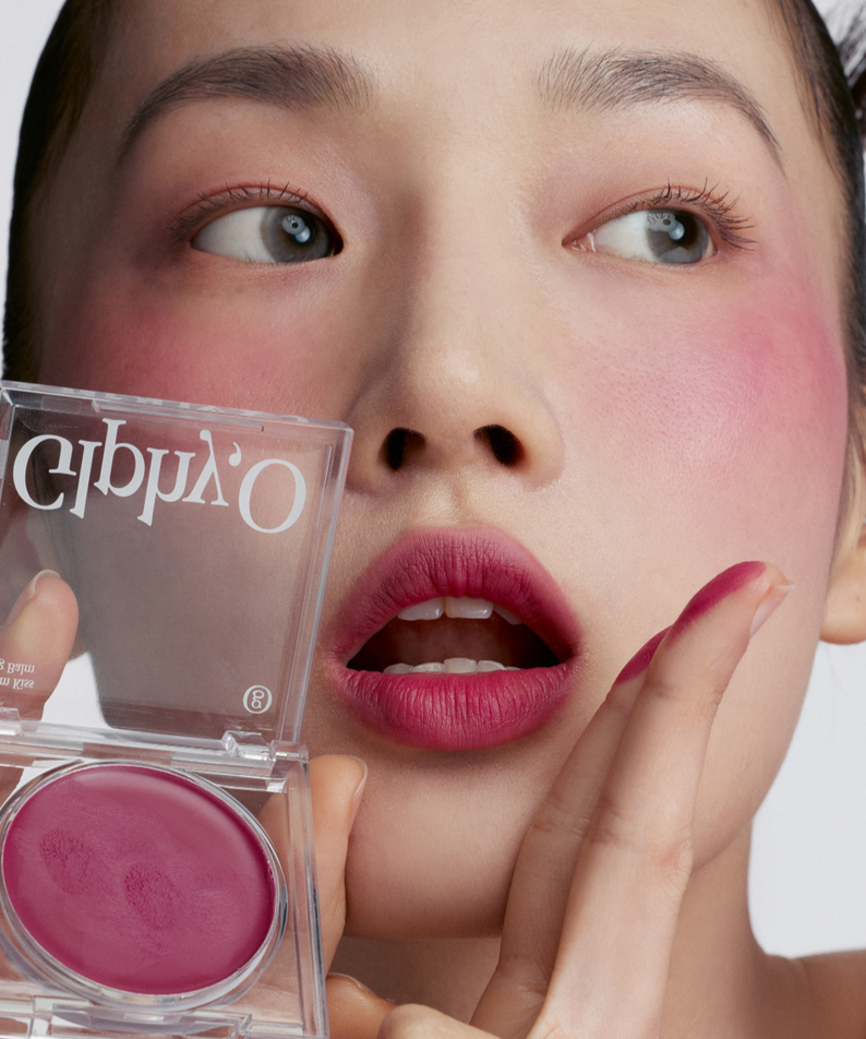 GLPHYO Fog Balm3.2g, marque GLPHYO : baume à lèvres en pot, maquillage rose sur le visage en gros plan, fond clair.