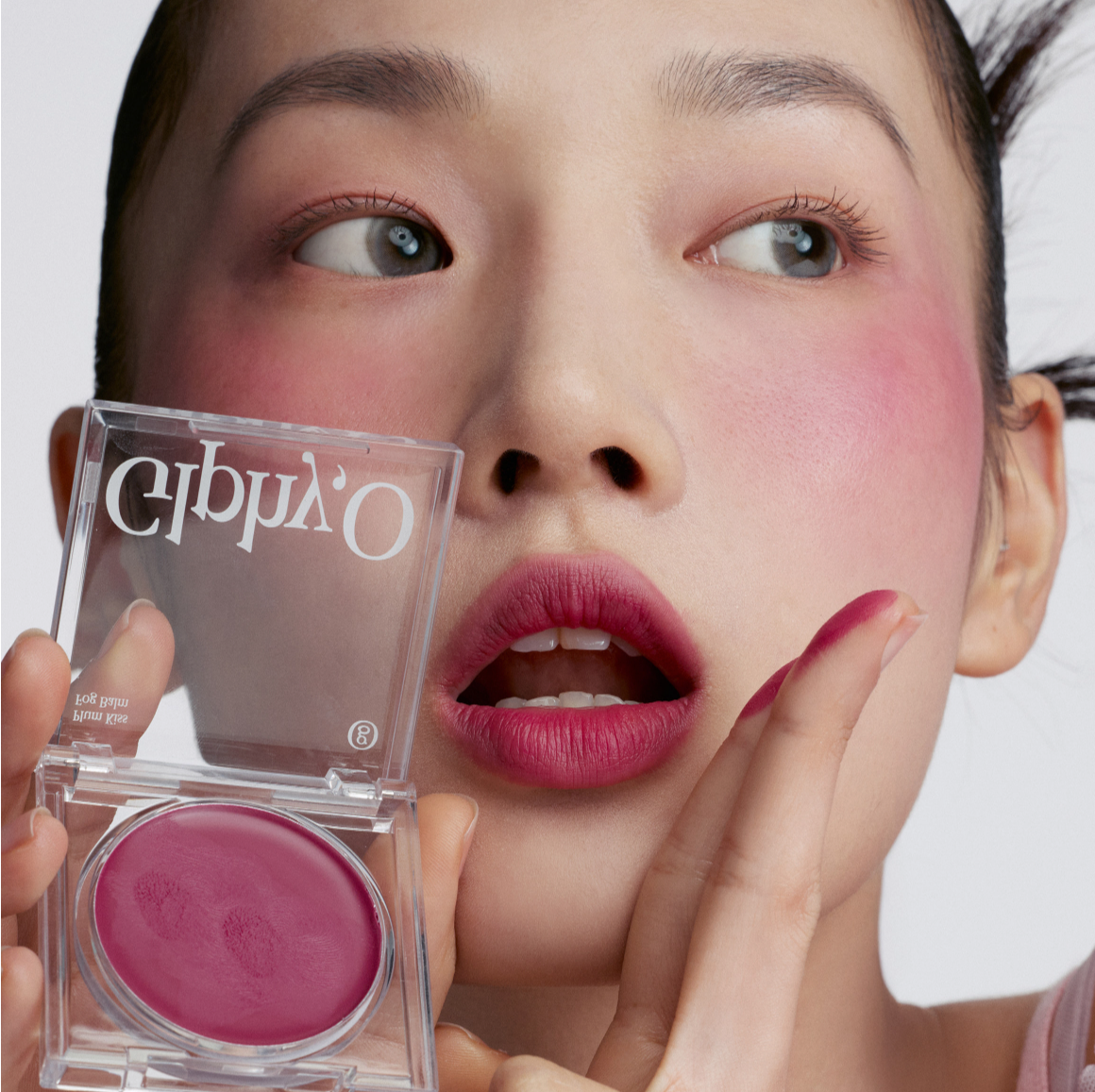 GLPHYO Fog Balm3.2g, marque GLPHYO : baume à lèvres en pot, maquillage rose sur le visage en gros plan, fond clair.
