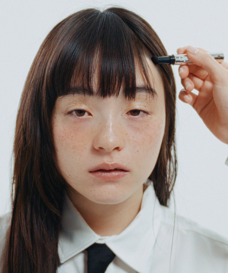 GLPHYO Hairline Maker 1.5g, appliqué sur la ligne de cheveux; main tenant le produit, jeune femme devant un fond clair.