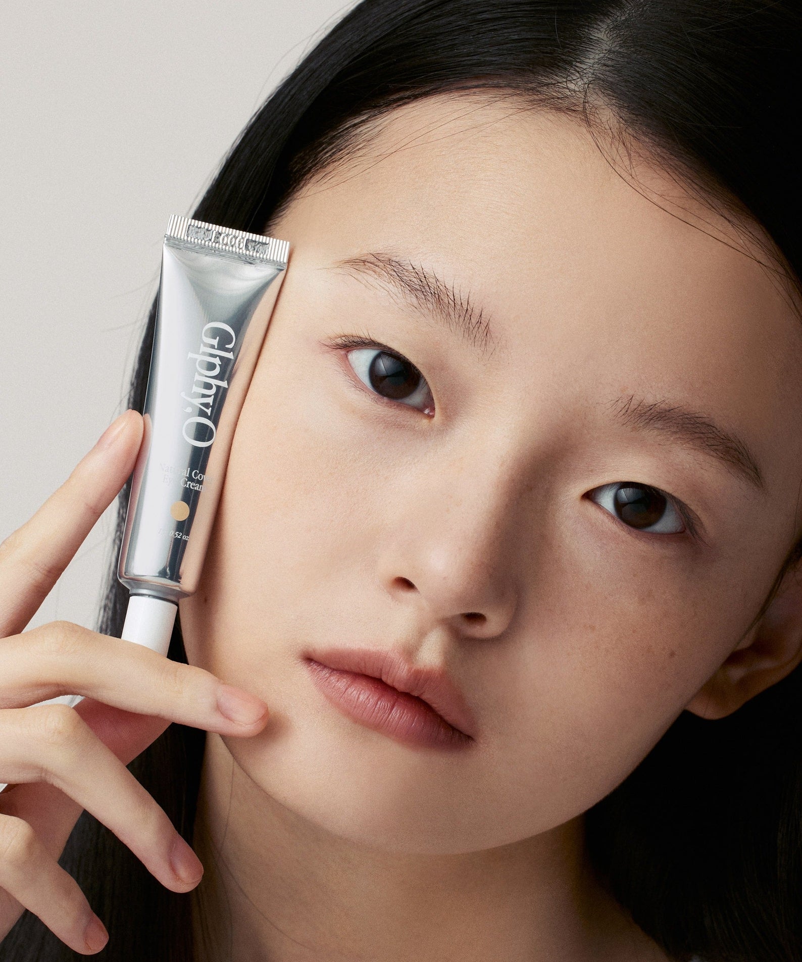 GLPHYO Natural Cover Eye Cream 15g de la marque GLPHYO : tube et femme, gros plan sur le contour des yeux, fond clair.