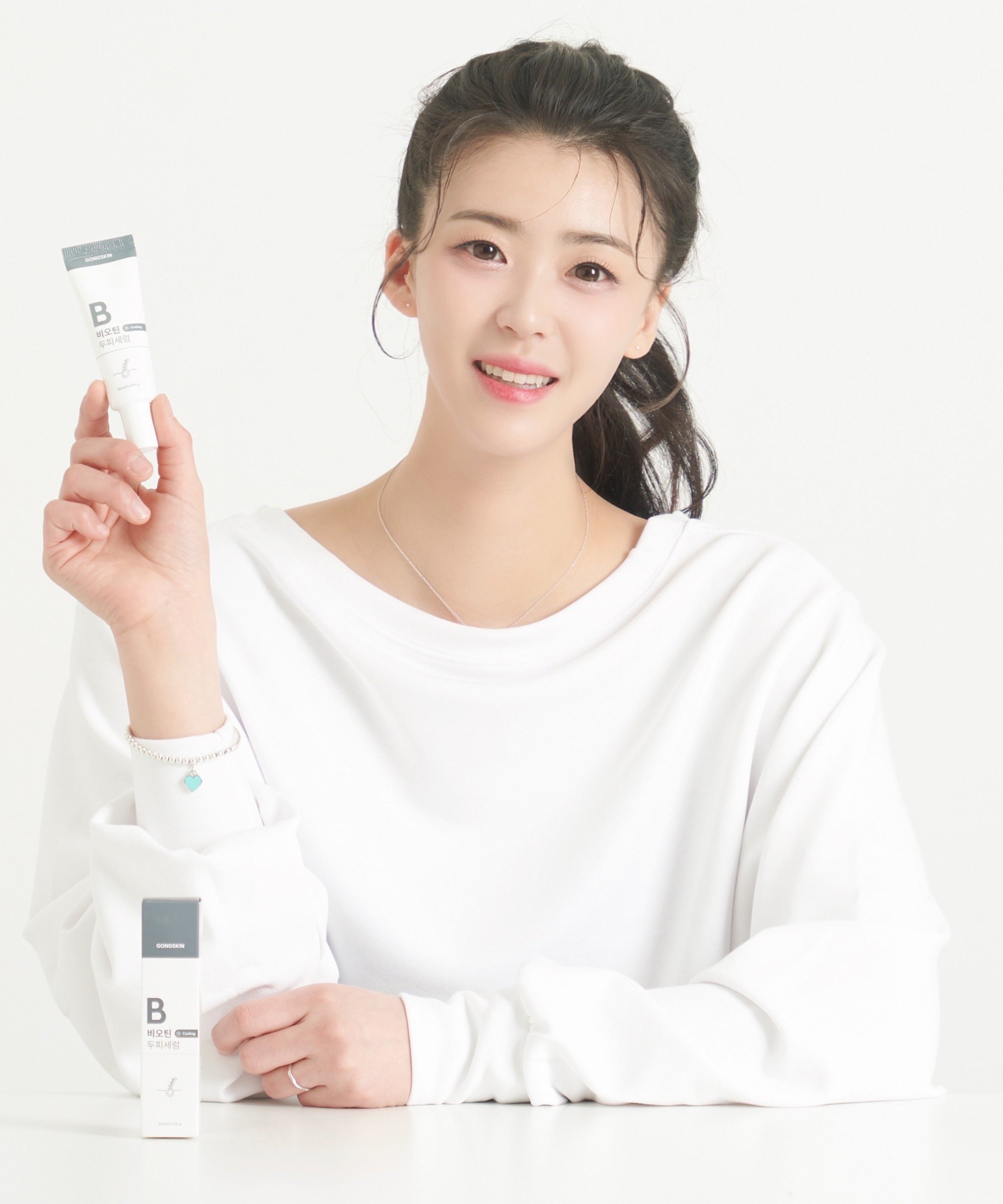 Décris l'image en français : GONGSKIN  Biotin Cooling Scalp Serum 20ml, marque montrée par une femme tenant le flacon sur fond clair.