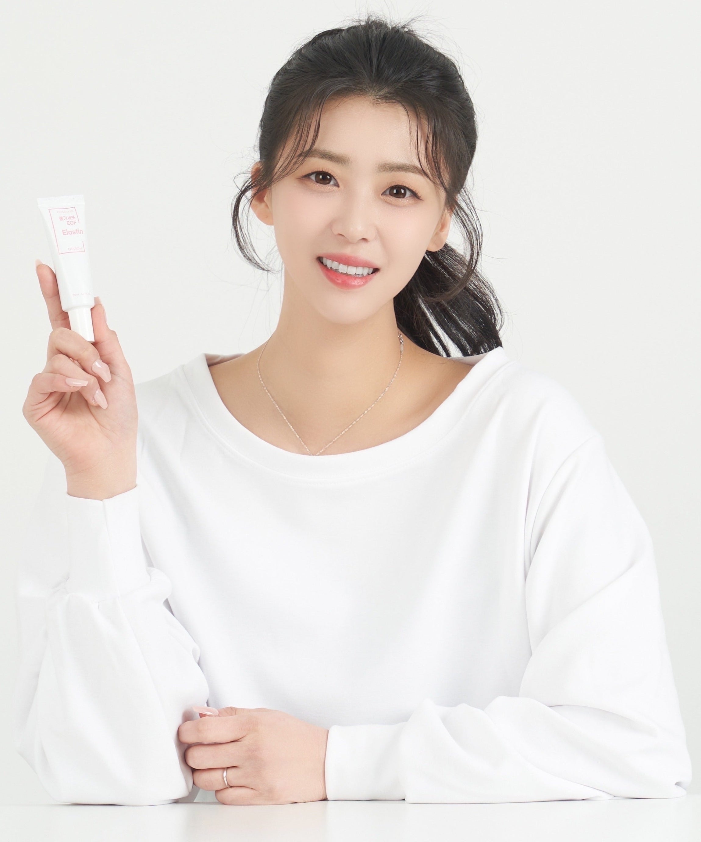Décris l'image en français : GONGSKIN  Stem Cell EGF Elastin Eye Cream 20ml, tube tenu par une femme souriante, fond clair.