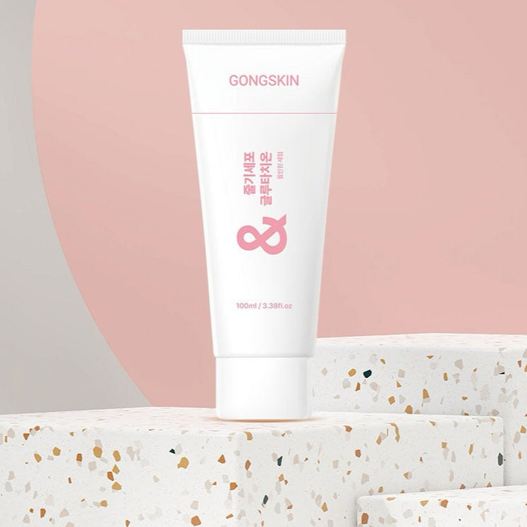Décris l'image en français : GONGSKIN  Stem Cell Glutathione All-in-One Serum 100ml sur fond rose et socle décoré