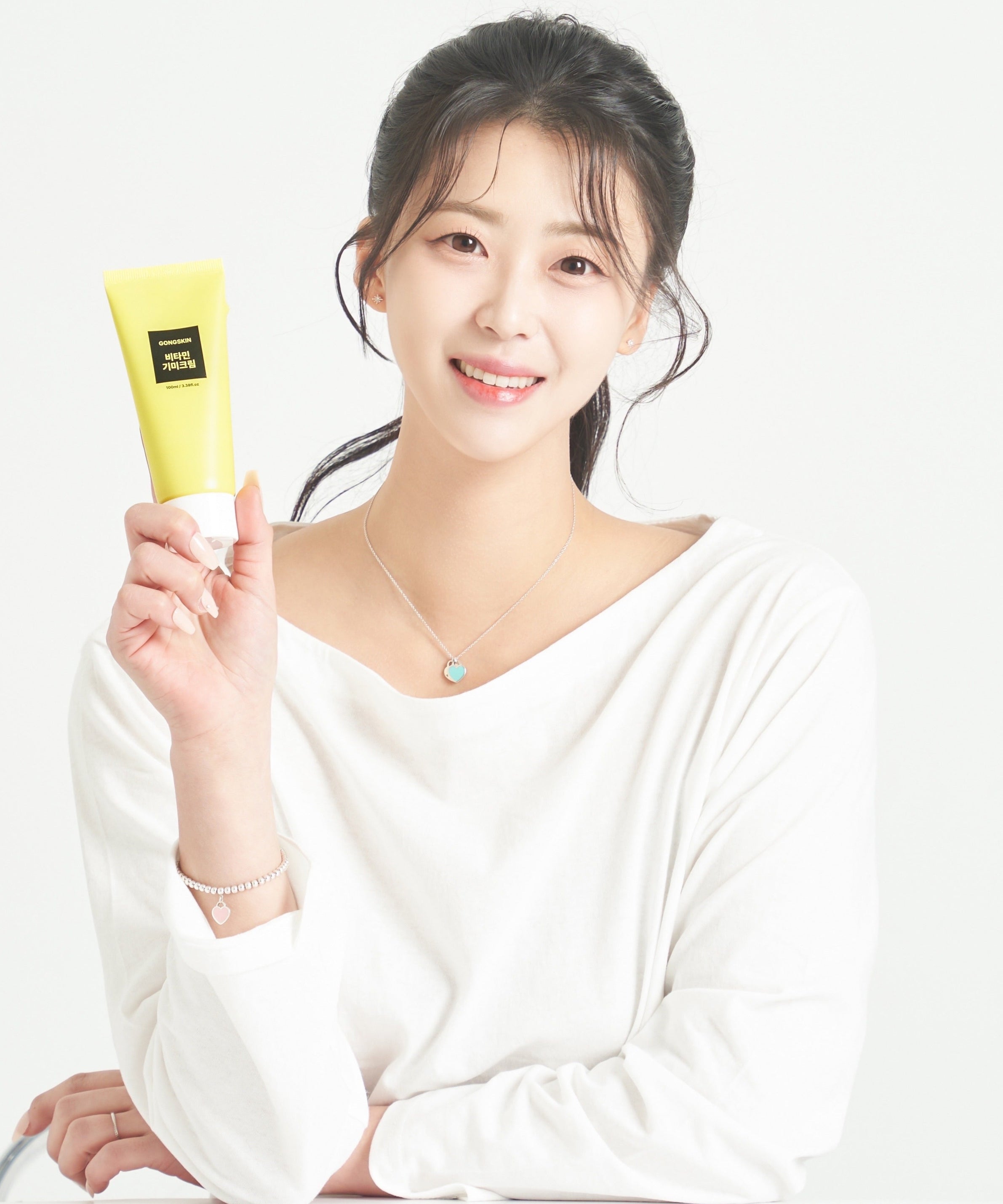 Femme souriante tenant un tube de crème GONGSKIN Vitamin Freckle Cream 100ml pour soin de la peau, posant en blouse blanche.