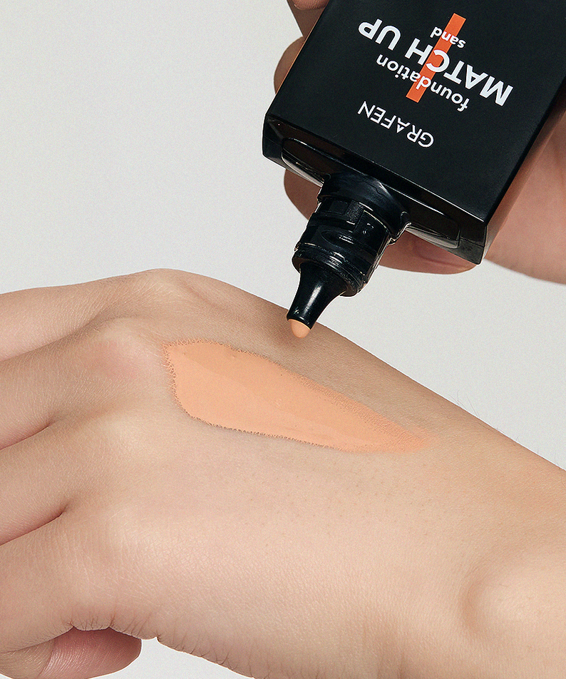 GRAFEN  Match Up Foundation 40ml : application de fond de teint sur peau, tube noir tenu à la main, contexte maquillage.