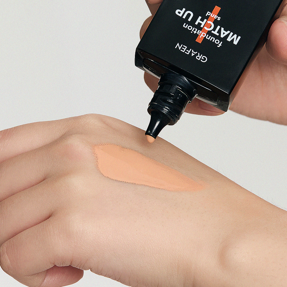GRAFEN  Match Up Foundation 40ml : application de fond de teint sur peau, tube noir tenu à la main, contexte maquillage.