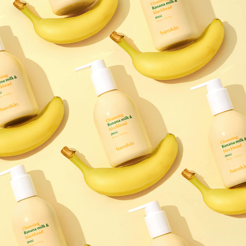 Décris l'image en français : HANSKIN Cleansing Banana Milk & Blackhead PHA 200ml, flacons et bananes sur fond jaune ensoleillé.