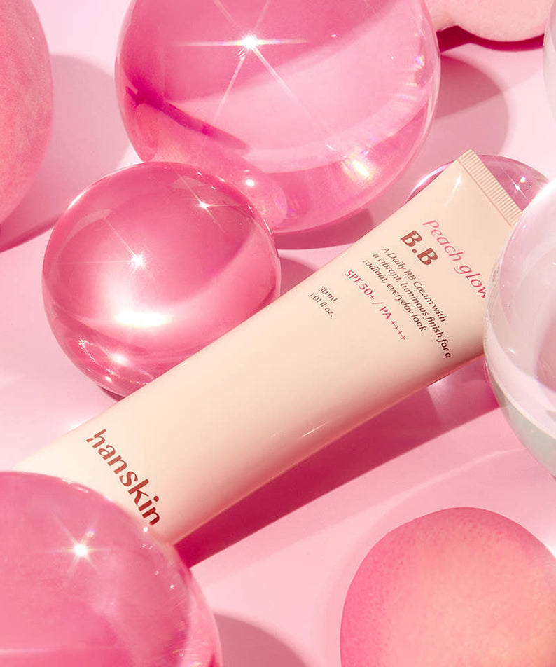 HANSKIN Peach Glow BB Cream 30ml de HANSKIN sur fond rose avec perles et cœurs, effet glow lumineux