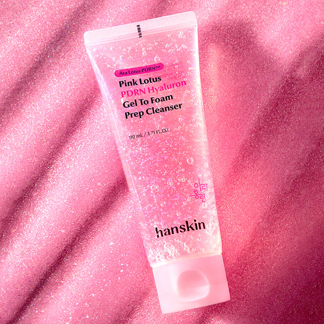 Décris l'image en français : HANSKIN Pink Lotus PDRN Hyaluron Gel to Foam Prep Cleanser 110ml, tube rose sur fond pailleté.
