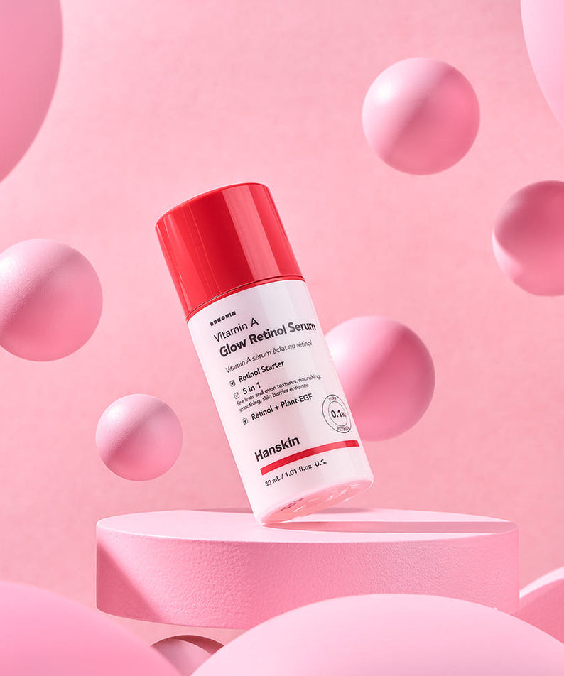 HANSKIN Vitamin A Glow Retinol Serum 30ml sur socle rose, marque HANSKIN, bouteilles et sphères décoratives, fond pastel.