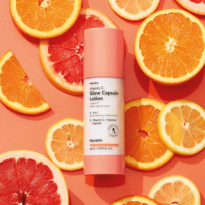 HANSKIN Vitamin C Glow Capsule Lotion 80ml de HANSKIN, flacon rose sur fond d’agrumes et capsules vitamine C
