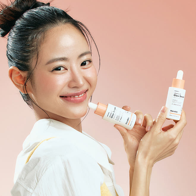 Photo de produit : HANSKIN Vitamin C Glow Serum 30ml par HANSKIN, flacon et femme en peau lumineuse sur fond rose.