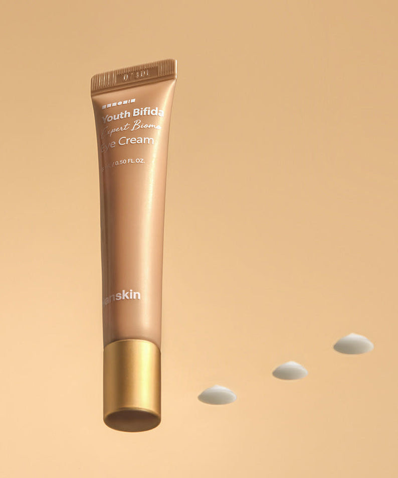 HANSKIN Youth Bifida Expert Biome Eye Cream 15ml de HANSKIN, tube beige sur fond sable, gouttes blanches.