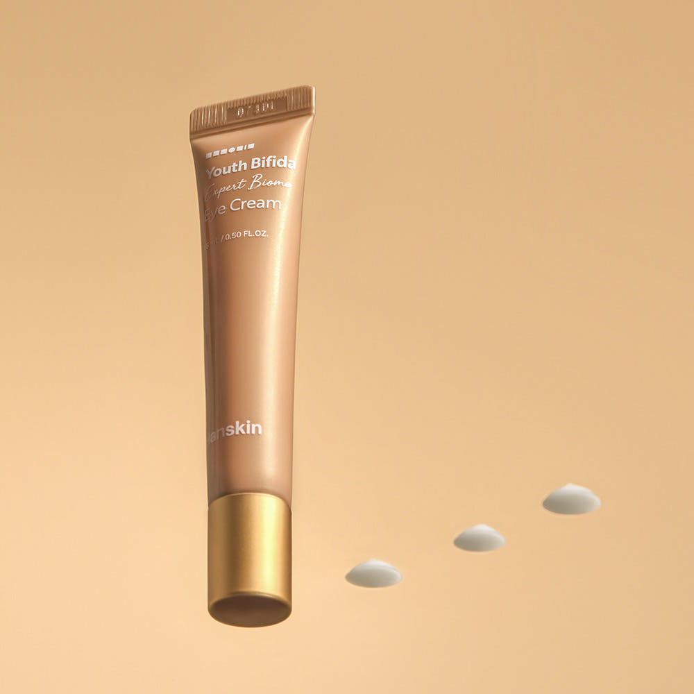 HANSKIN Youth Bifida Expert Biome Eye Cream 15ml de HANSKIN, tube beige sur fond sable, gouttes blanches.
