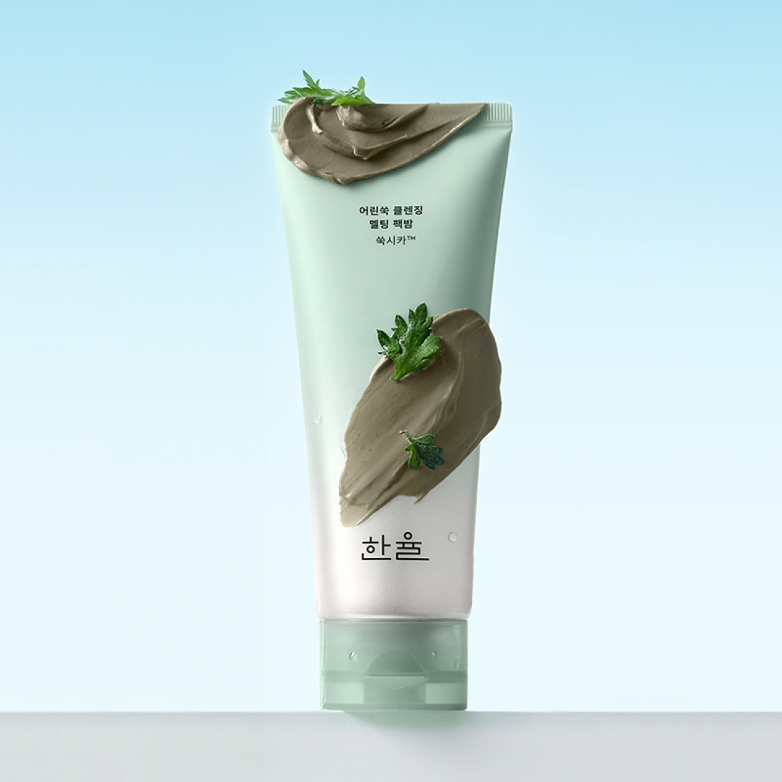 HANYUL Young Artemisia Cleansing Pack Balm 100g : tube de baume nettoyant sur fond bleu, textures d’armoise et herbes vertes.