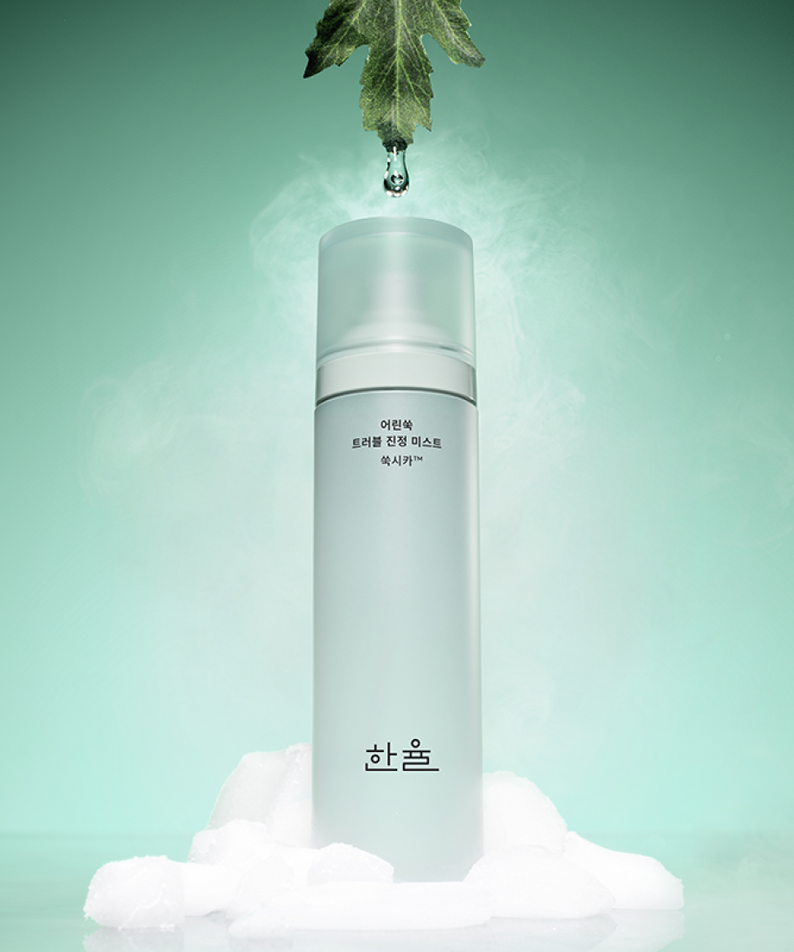 HANYUL Young Artemisia Trouble Mist 120ml posé sur de la glace, sur fond vert avec une feuille suspendue au-dessus.