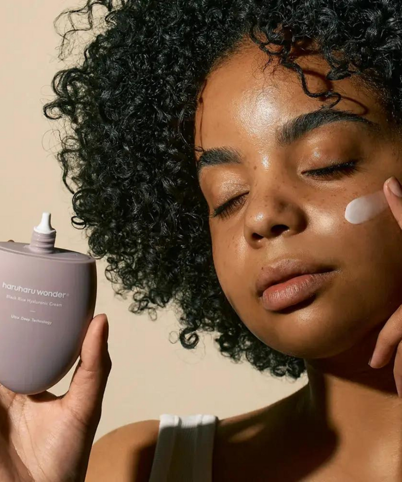 HARUHARU Black Rice 10 Hyaluronic Cream 50ml, femme aux cheveux bouclés appliquant la crème hydratante, tube et pot.