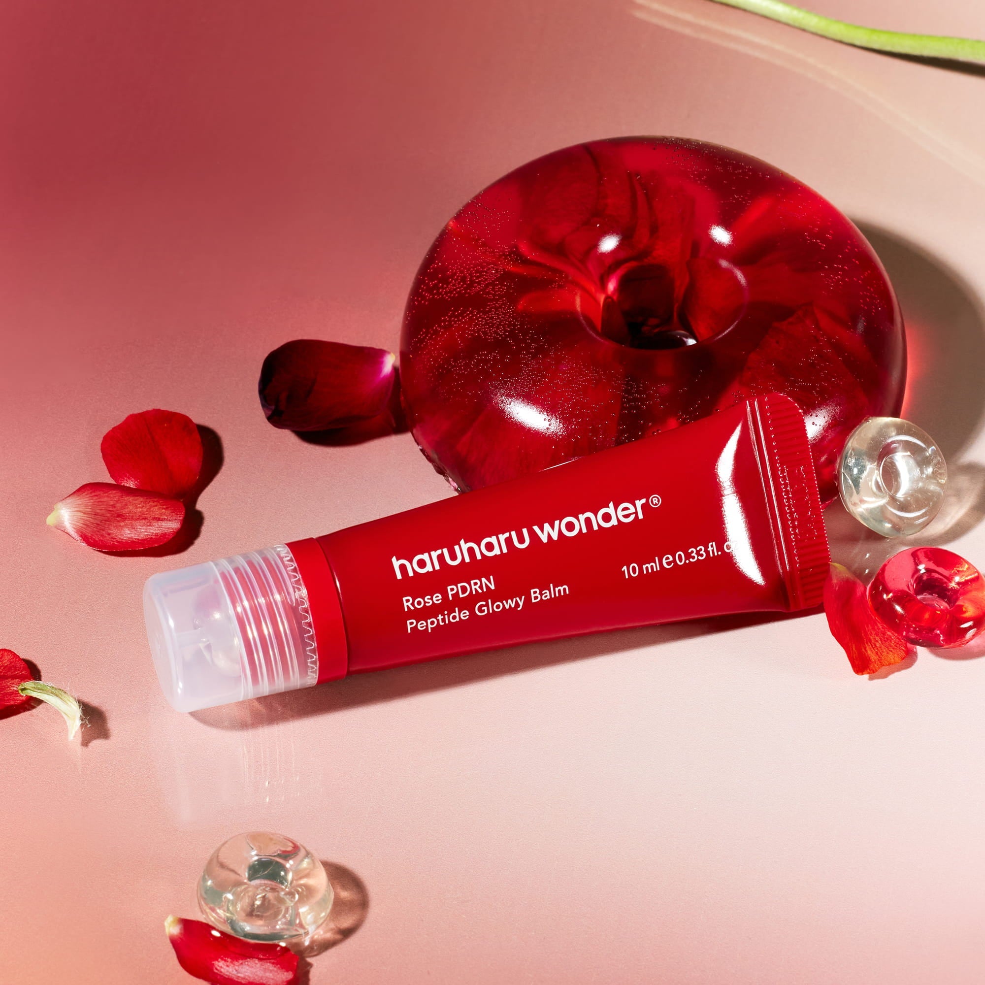 HARUHARU Rose PDRN  Peptide Glowy Balm 10ml, tube rouge sur fond rose, marque HARUHARU, fleurs et gouttes de sérum