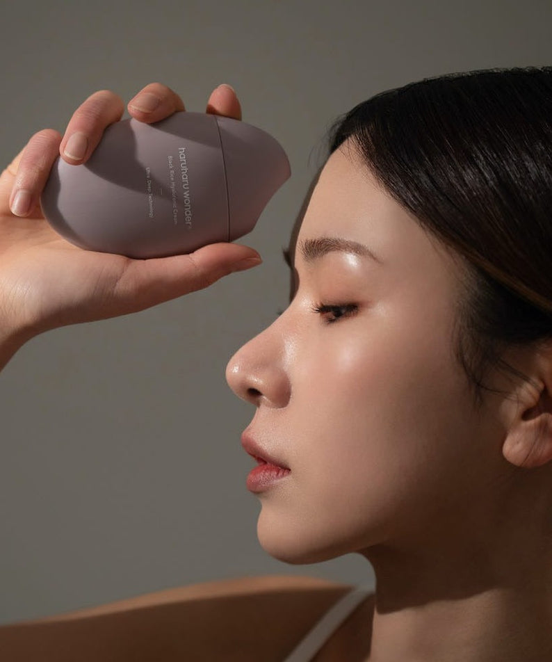 Femme tenant le HARUHARU Black Rice 10 Hyaluronic Cream 50ml près de son visage pour soin de la peau.