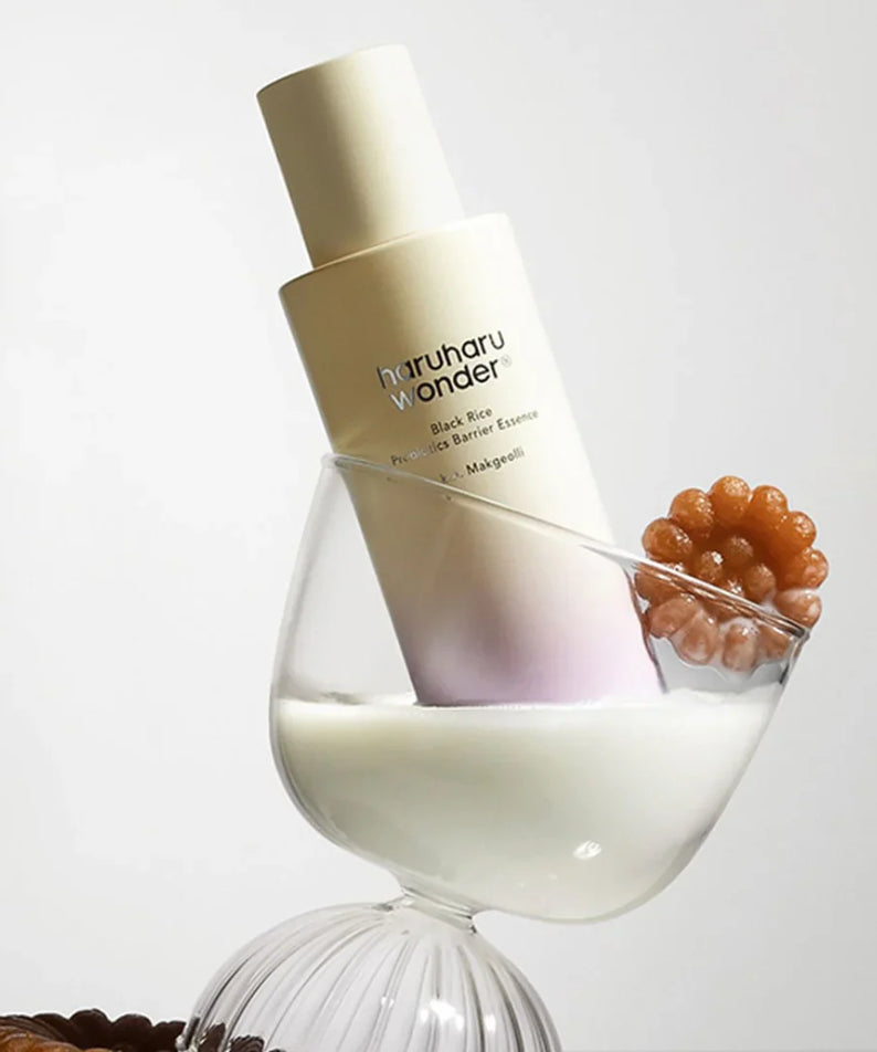 Flacon de HARUHARU Black Rice Probiotics Barrier Essence 120ml sur fond créatif avec structure en verre et éléments décoratifs.