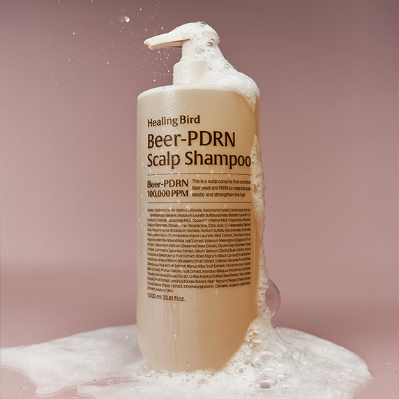 Décris l'image en français : HEALING BIRD Beer PDRN Anti-Hair Loss Shampoo 1000ml, flacon blanc sur fond rose, mousse