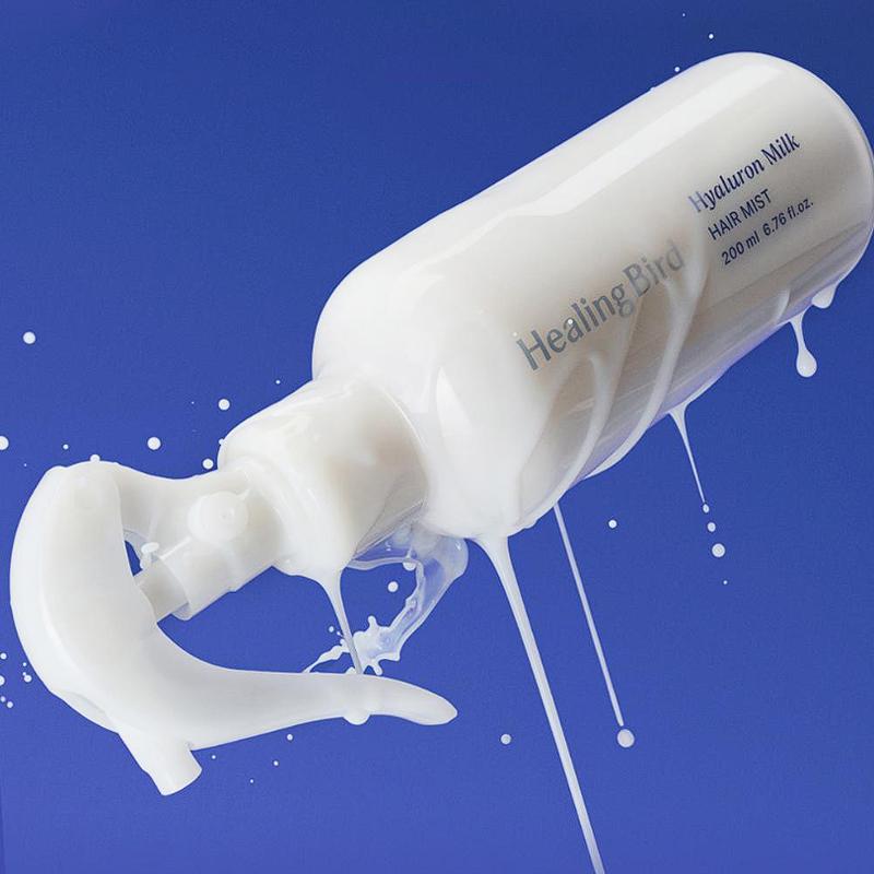 Décris l'image en français : HEALING BIRD Hyalutonic Milk Hair Mist 200ml, brume crème, marque sur flacon, fond bleu.