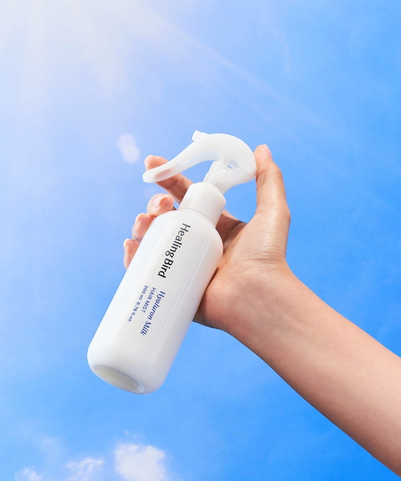 HEALING BIRD Hyalutonic Milk Hair Mist 200ml tenu dans la main devant un ciel bleu ensoleillé, soin hydratant pour cheveux.