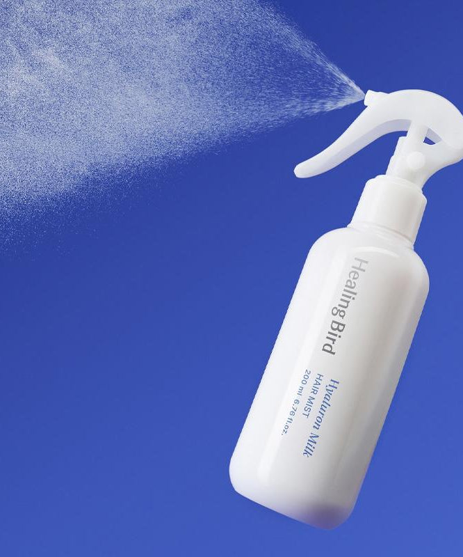 Flacon blanc de HEALING BIRD Hyalutonic Milk Hair Mist 200ml vaporisant une brume, fond bleu vibrant.