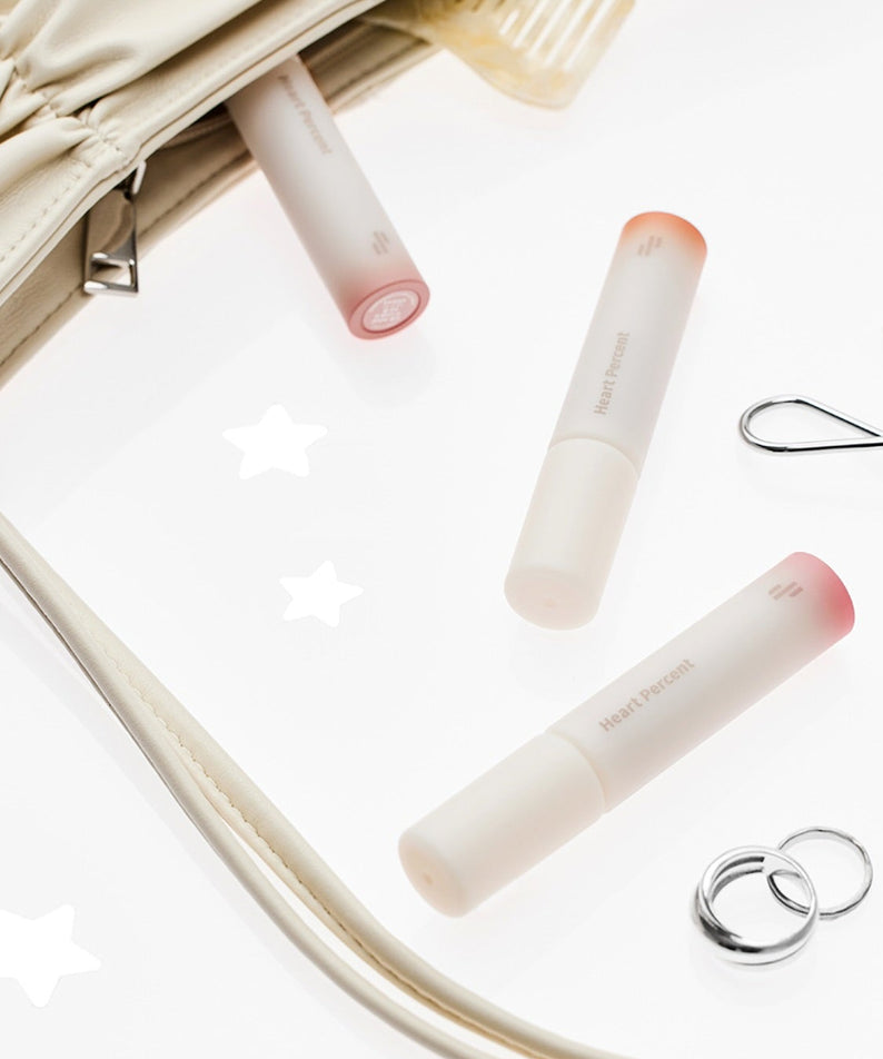 HEART PERCENT Dot On Mood All Cover Lip Base, baume à lèvres élégant, bague, recourbe-cils, sac, sur fond blanc avec étoiles.