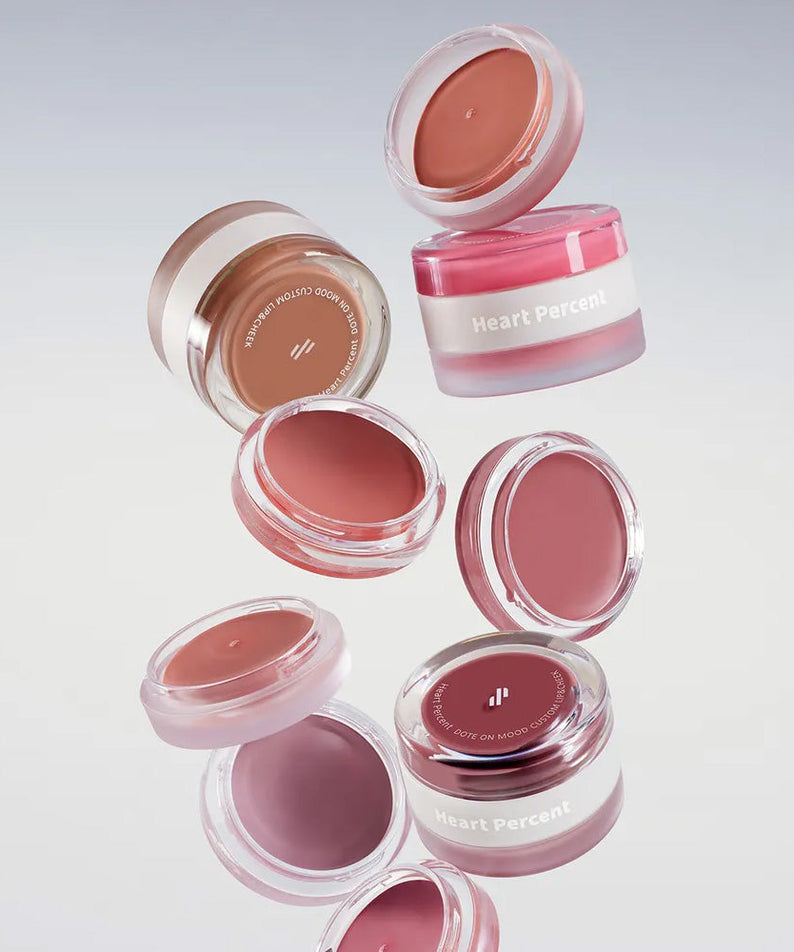 Produits colorés HEART PERCENT Dot On Mood Custom Lip & Cheek en lévitation, parfaits pour lèvres et joues.