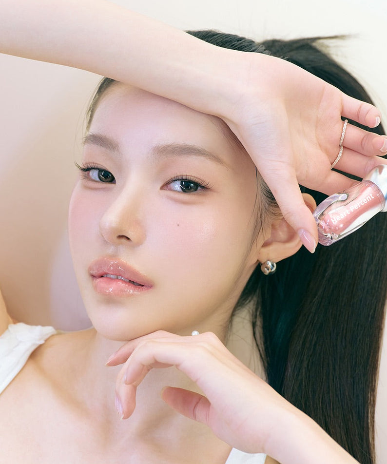 HEART PERCENT Dot On Mood Over Melting Gloss sur fond clair : maquillage lèvres, peau rosée, main et visage modèle.
