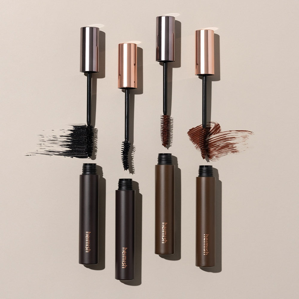 HEIMISH Dailism Mascara de la marque HEIMISH, brosses et tubes maquillage sur fond beige, gros plan.