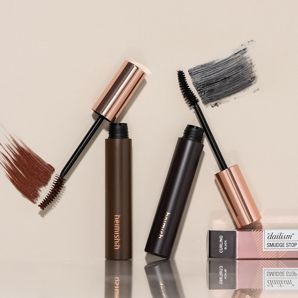 Décris l'image : HEIMISH Dailism Mascara, marque HEIMISH, avec brosses et étui, fond beige minimal.