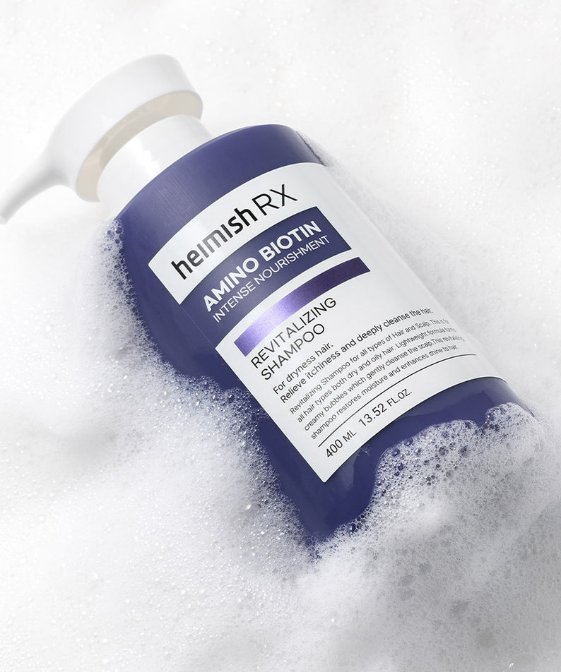 Bouteille de HEIMISH RX Amino Biotin Revitalizing Shampoo 400ml sur fond de mousse savonneuse.